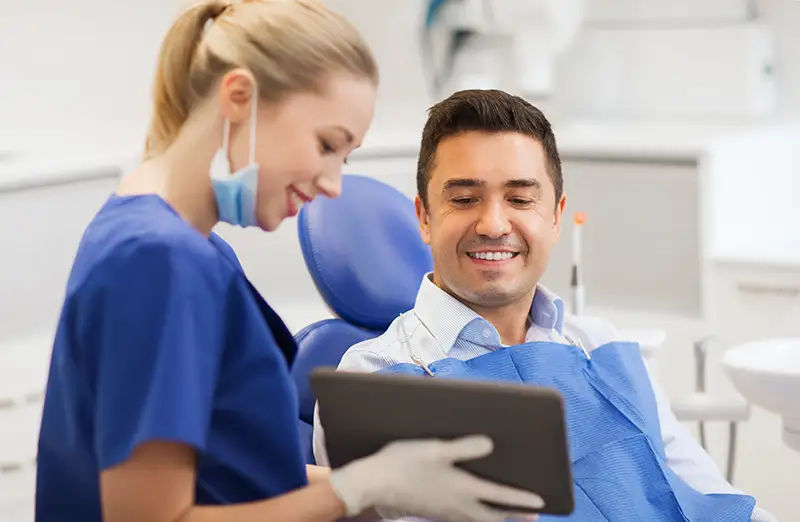 A dentist counseling a patient in the chair with an electronic tablet in hand