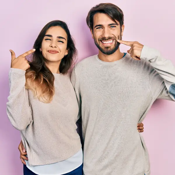 A young man and woman pointing at their smiles 