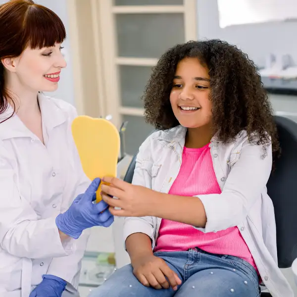 A female dentist holding up a mirror to smiling young patient 