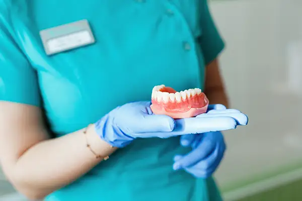 Close-up of a dental assistant in gloves presenting a set of dentures to demonstrate their design and function.