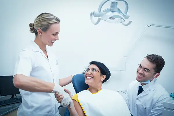A woman smiling and shaking hands with her dentist and a dental hygienist to the side.