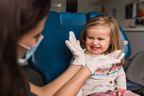 A young girl making a silly smile at the dental hygienist during her exam, highlighting fun and comfort.