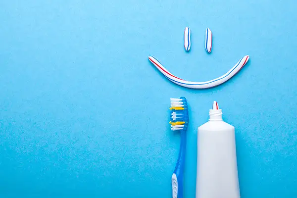 Toothbrush and toothpaste creating a smile shape on a blue background, promoting oral care and hygiene.